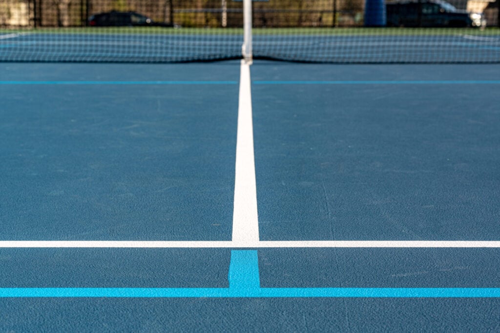 Blue tennis court with white lines and light blue pickleball lines.