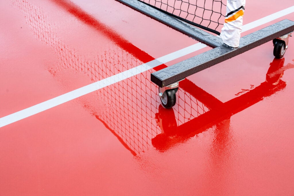 New portable pickleball nets on a wet red tennis court with white lines combined with gray pickleball lines