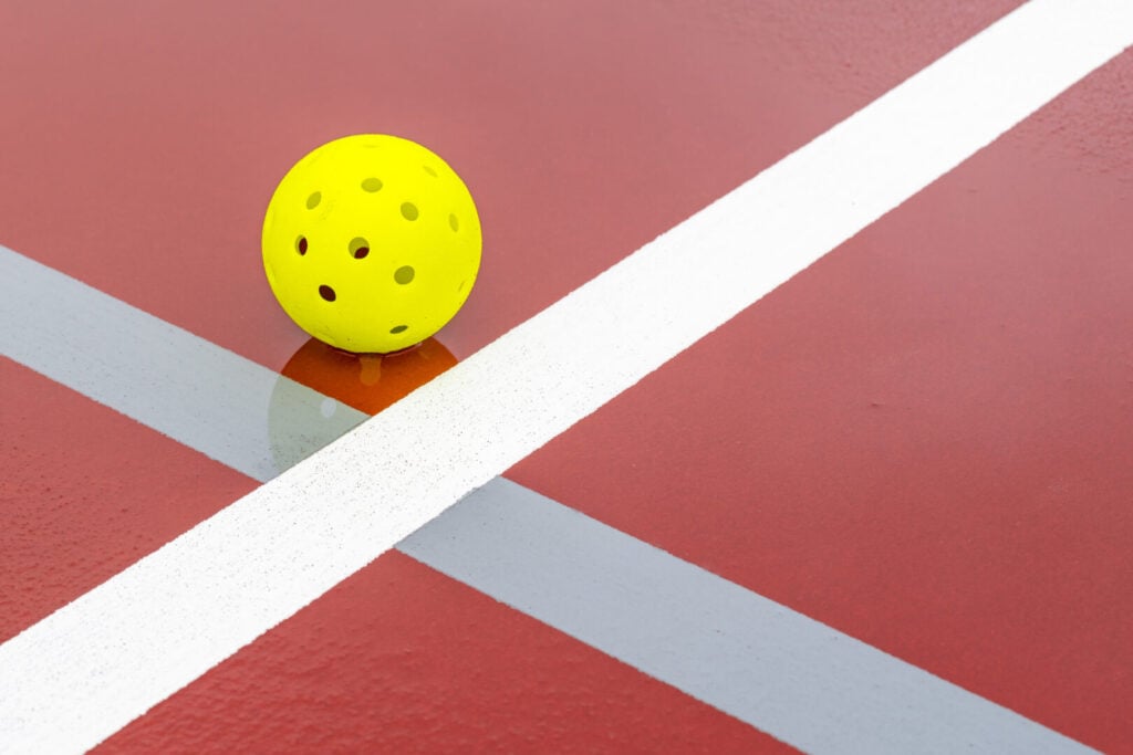 A pickleball on a wet red pickleball tennis court with white lines combined with gray pickleball lines